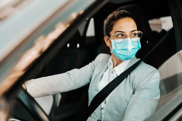 Fototapeta na wymiar Young cute brunette dressed smart casual with face mask on driving her car during corona virus outbreak.