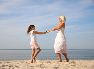 Cute little girl with grandmother spending time together on sea beach