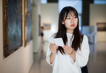 Chinese woman standing with guide-book in art museum near the painting in baguette