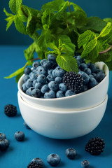 White bowl with mix blueberry, blackberry and mint leaves on blue background.