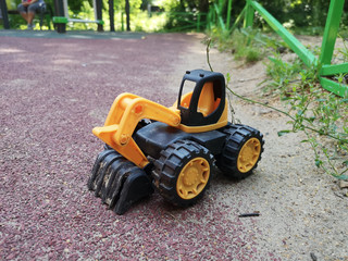 Small toy yellow excavator on rubber playground.