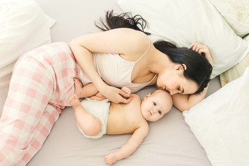 Happy young mother and cute baby in bed. Light background.