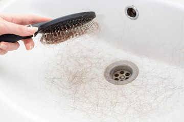 A females hand holds a comb with a bunch of torn hair over the sink. Hand close-up. The concept of baldness and hair care