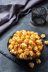 Popcorn in caramel glaze in a plate on a dark concrete table. Copy space.