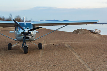 A small silver plane landed on the sandy shore of a river island during the summer sunset.