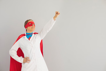 Young doctor in superhero costume ready to fight diseases, grey background. Medical worker against...