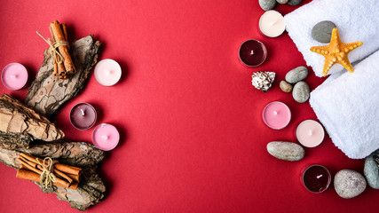 Spa still life treatment with candles, stones, sea shells starfish cinnamon bark and towels on red...