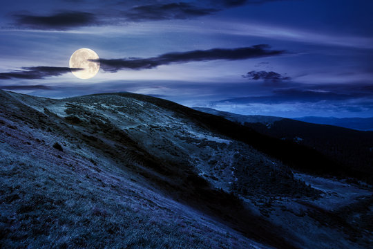 hills and valley of mountain landscape at night. clouds on the deep blue sky. beautiful scenery of chornohora ridge in full moon light