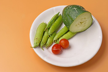 Cherry tomatoes, pea pods and a sliced cucumber on a plate on an orange background close-up