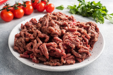 Fresh ground beef on a plate. Finely chopped raw meat on a plate with spices, tomatoes and herbs is ready for cooking.