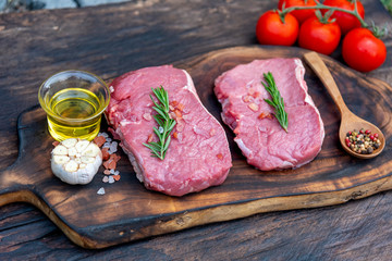 Raw meat beef steak organic fresh ingredient on wooden board table background in kitchen with rosemary, salt, garlic, tomato, black pepper, olive oil. Meat beef on wooden plate for beefsteak raw meat