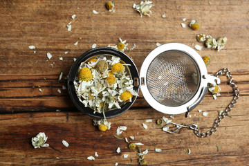 Obraz na płótnie Canvas Dry chamomile flowers in infuser on wooden table, flat lay