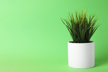 Beautiful artificial plant in flower pot on green background, space for text