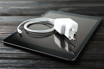 Tablet and charging cable with adapter on black wooden table