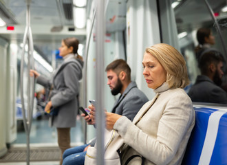 Fototapeta na wymiar Modern middle aged woman traveling in metro car and using mobile phone..