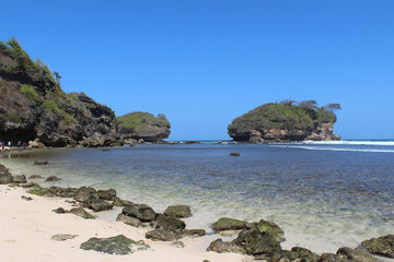 Obraz premium beautiful watu karang beach in Pacitan, with a background of blue sky with clouds, rock and white sands, East Java, Indonesia