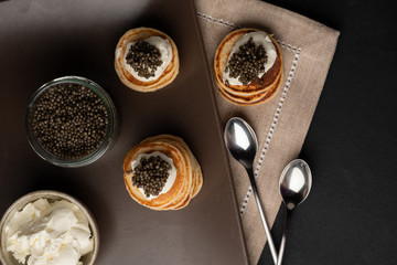 Black caviar, curd cheese, mini pancakes, blackberries on a wooden background.