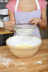 Woman sieving flour into mixing bowl