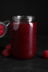 Delicious jam and fresh raspberries on black slate table, closeup