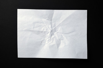 A sheet of crumpled white paper on a black background.Crumpled white paper background. Wrinkled sheet texture, top view.