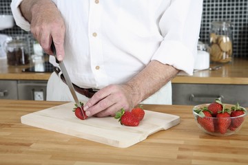 Senior man cutting strawberries in the kitchen