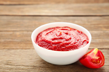 Tomato ketchup sauce in a bowl with tomatoes on grey wooden background. View from above.