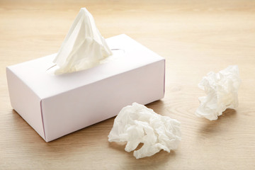 Box with paper tissues and used crumpled napkins on light background