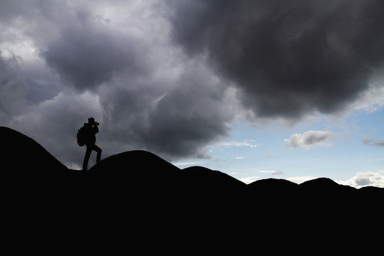 Silhouette of a man with backpack in the mountains is taking pictures of the landscape