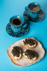 Fototapeta na wymiar Sandwiches with black caviar and coffee in blue cups on a blue background.