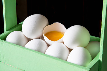 Close-up of fresh white organic chicken eggs and egg yolk in the green wooden box on dark wooden background