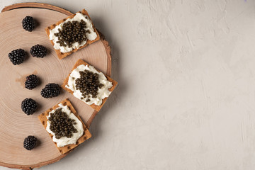 toast with curd cheese, caviar and blackberries on the saw cut of the tree on a gray background