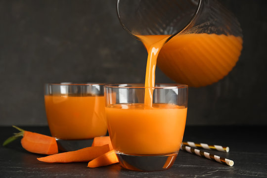 Pouring freshly made carrot juice into glass on black table