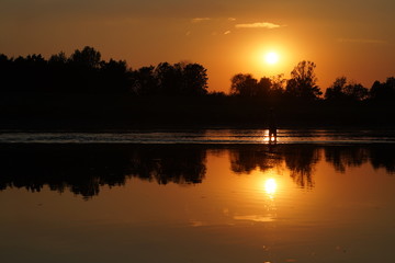 Fototapeta premium Fisherman fishing at sunset, sun reflecting in water