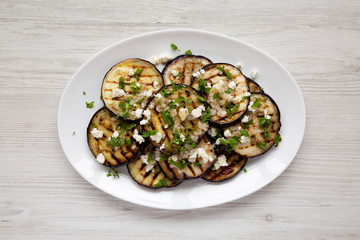 Homemade Grilled Eggplant with Feta and Herbs on a white plate on a white wooden background, top view. Flat lay, overhead, from above.