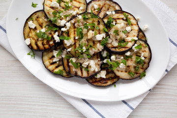 Homemade Grilled Eggplant with Feta and Herbs on a white plate, top view. Flat lay, overhead, from above. Close-up.