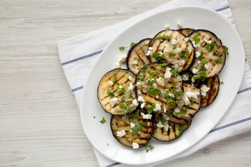 Homemade Grilled Eggplant with Feta and Herbs on a white plate, top view. Flat lay, overhead, from above. Copy space.