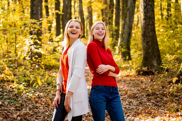 Naklejka na ściany i meble Two girls outdoors enjoying Autumn nature. Portrait of friends women on maple leaves.