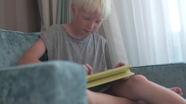 A beautiful blonde boy plays in a tablet in a hotel room.