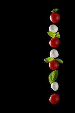 Vertical composition of mozzarella cheese, fresh cherry tomato and basil leaves isolated on a black background with reflection, healthy food concept, horizontal image with space for text.