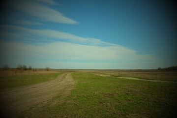 Dirt road in the fields on a spring day. Country landscape. Beautiful cloudy sky over the field. Vignette.