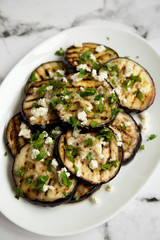 Homemade Grilled Eggplant with Feta and Herbs on a white plate on marble background, side view.