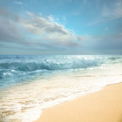 Fototapeta na wymiar Ocean waves rolling on sandy beach under blue sky with clouds