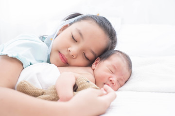 little sister hugging her newborn brother. toddler kid meeting new sibling. love, trust and tenderness. cute girl and new born baby boy relax in a white bedroom. family with children at home.