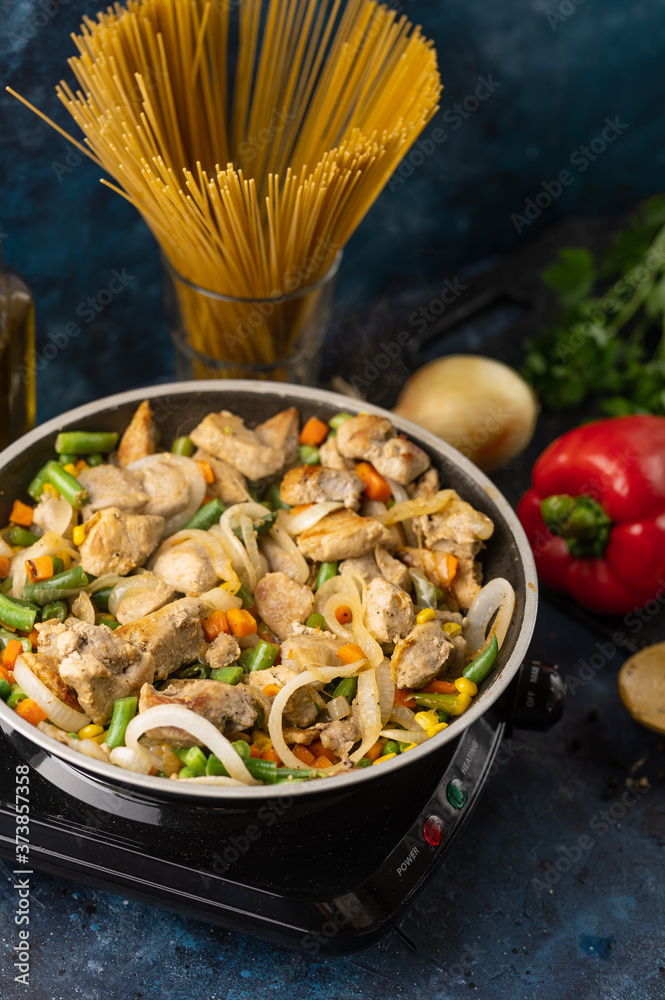 Wall mural Pork meat is fried in a pan with vegetables on the background of vegetables and italian pasta, culinary recipes