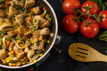 Pork meat is fried in a pan with vegetables on the background of vegetables and italian pasta, culinary recipes