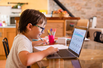 Little boy doing homework on laptop at home.