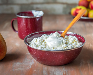 Breakfast with cottage cheese in a deep enamel cup and a wooden spoon, a mug with sour cream and nectarines