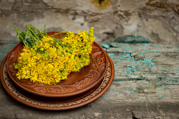 Wildflowers in a brown ceramic plate on an old wooden table top; summer layout