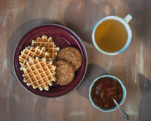 Morning tea with cookies, waffles and apple jam on the brown table