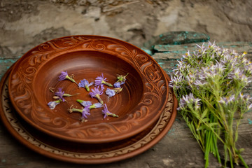 Wildflowers in a brown ceramic plate on an old wooden table top; summer layout